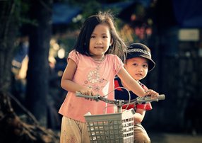 Young asian girl walking bike with baby brother